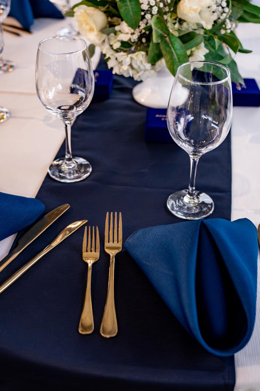 Detalle de copas y cubiertos dorados sobre mantel azul marino