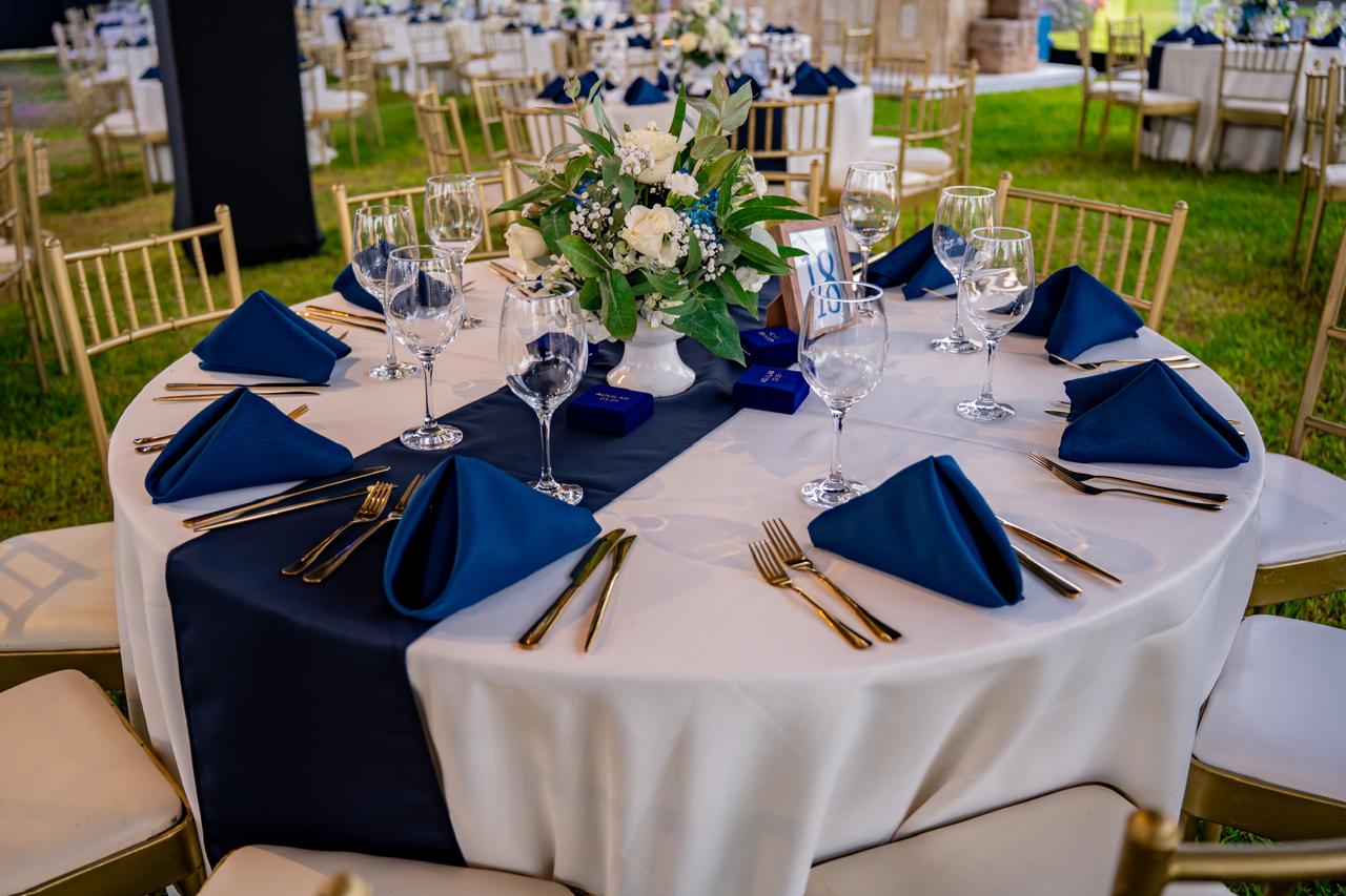 Mesa redonda montada en jardín con mantelería blanca y azul