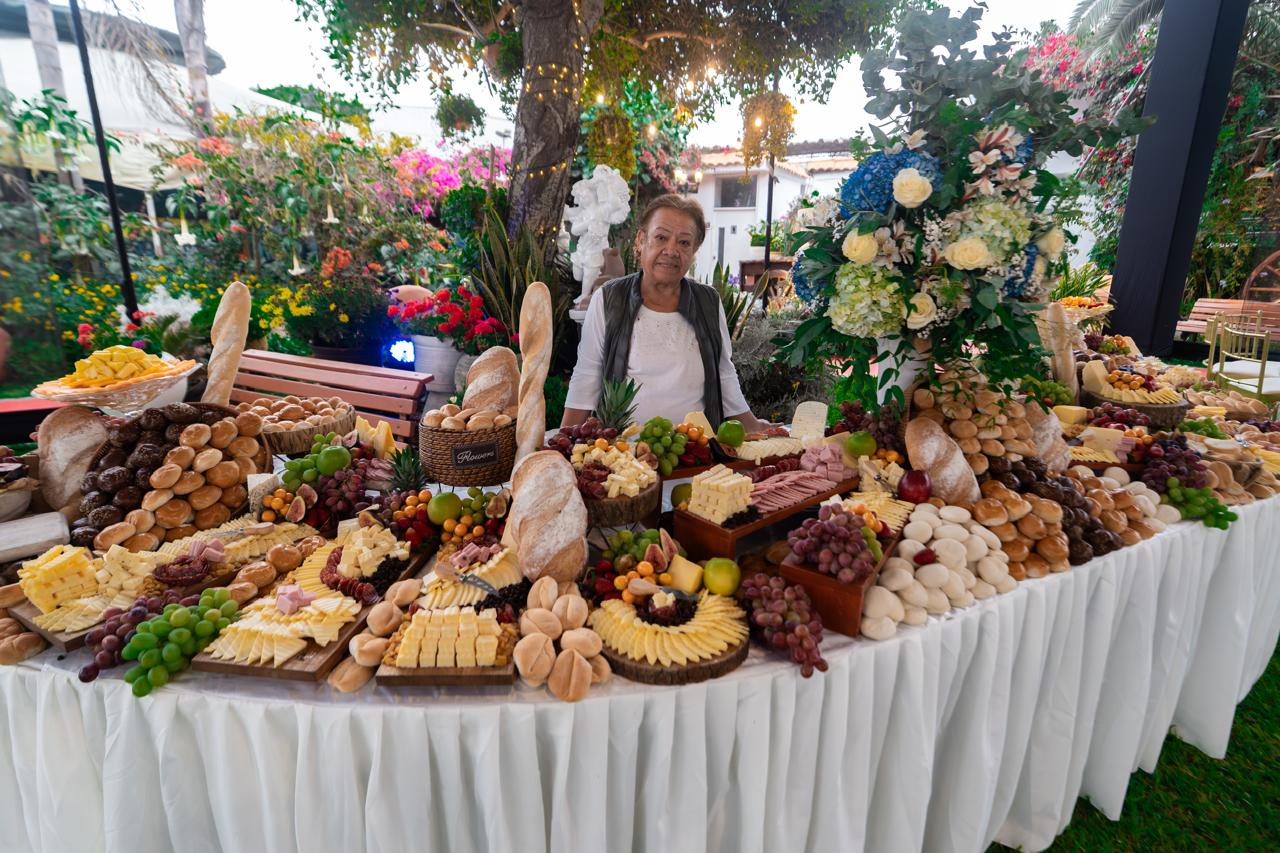 Mesa de buffet completa con panes, quesos y flores en jardín